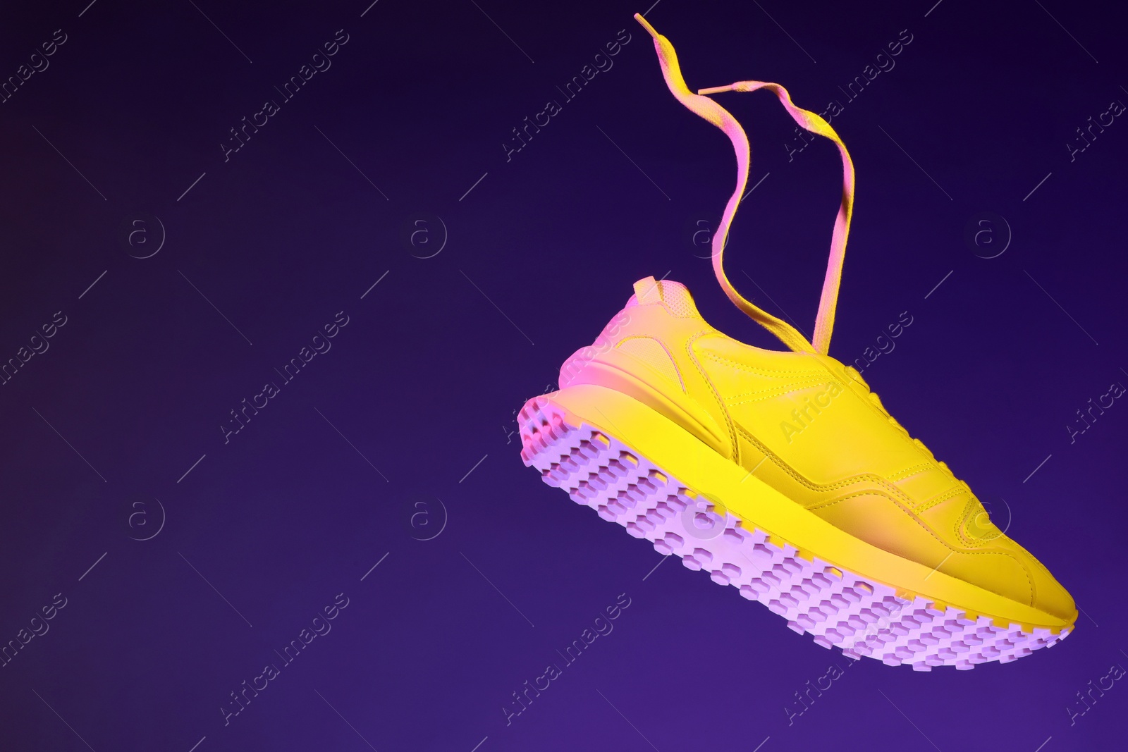 Photo of Stylish sneaker in air against dark purple background in neon lights, space for text