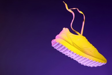 Stylish sneaker in air against dark purple background in neon lights, space for text