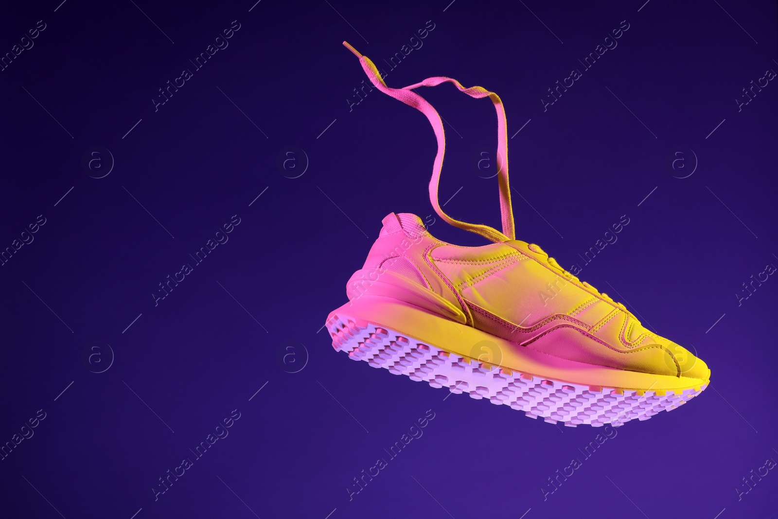 Photo of Stylish sneaker in air against dark purple background in neon lights, space for text