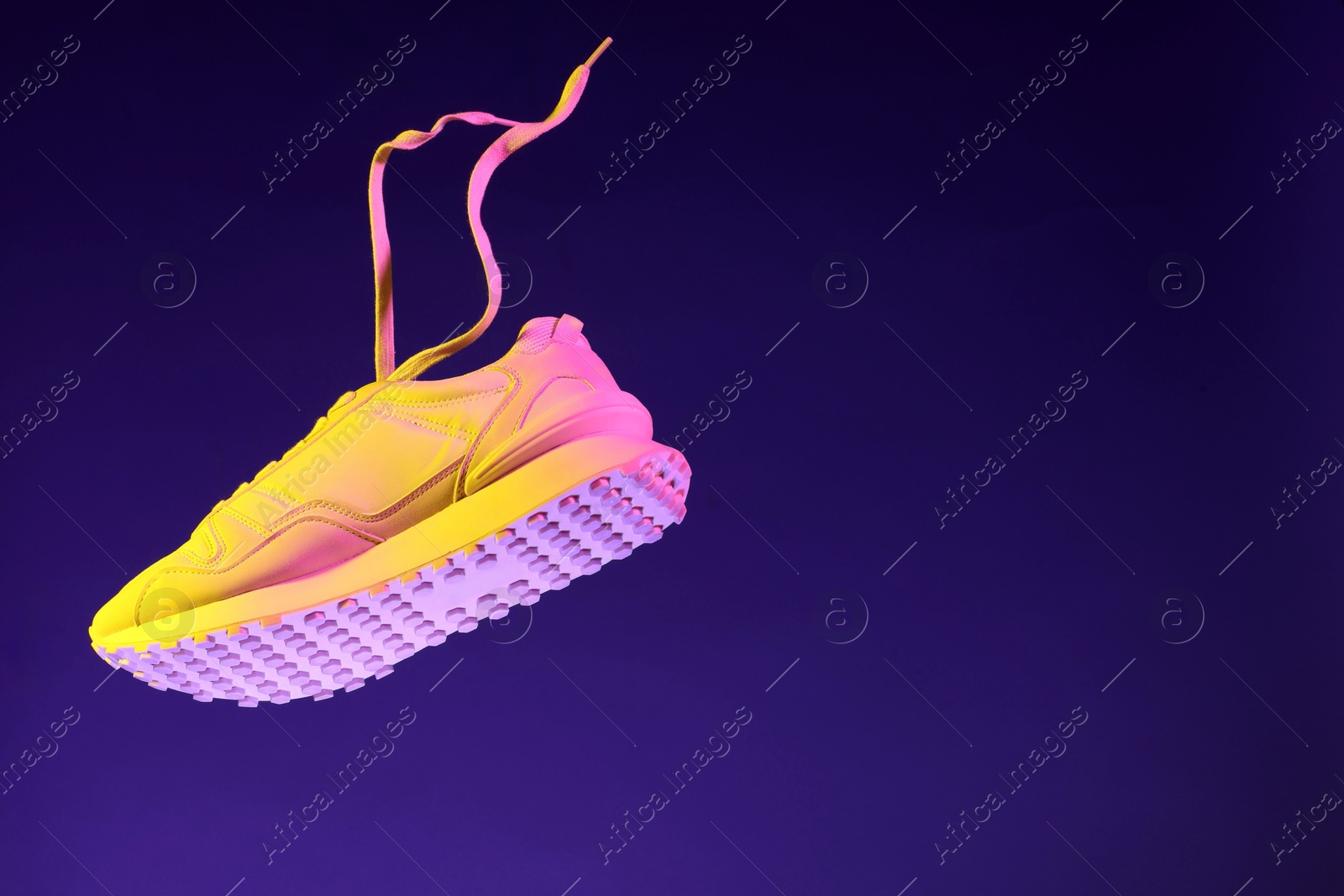 Photo of Stylish sneaker in air against dark purple background in neon lights, space for text