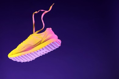 Photo of Stylish sneaker in air against dark purple background in neon lights, space for text