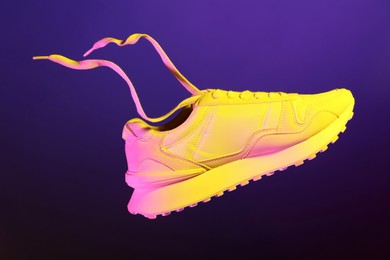 Photo of Stylish sneaker in air against dark purple background in neon lights