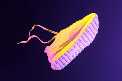 Photo of Stylish sneaker in air against dark purple background in neon lights