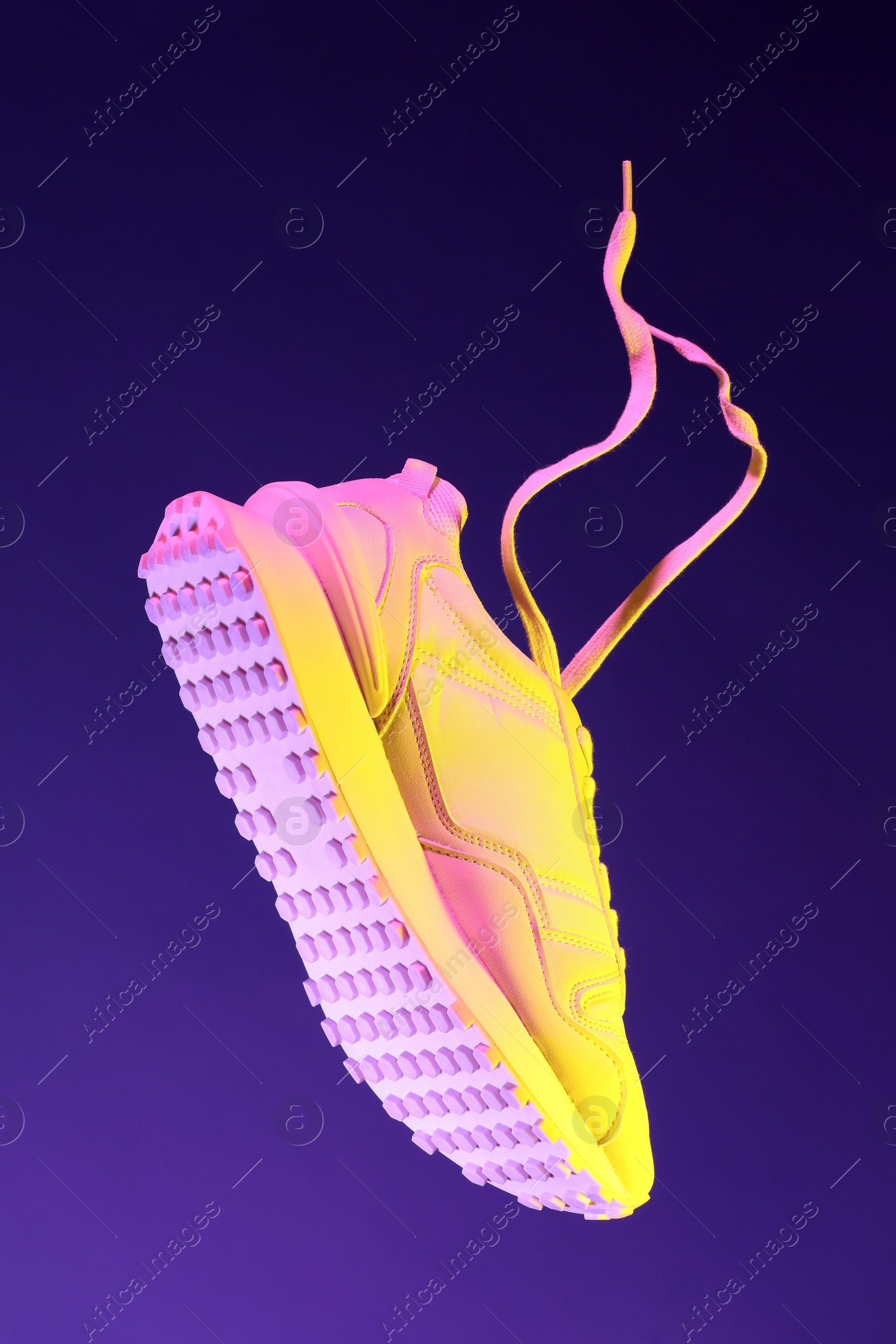 Photo of Stylish sneaker in air against dark purple background in neon lights