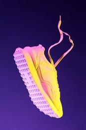 Photo of Stylish sneaker in air against dark purple background in neon lights