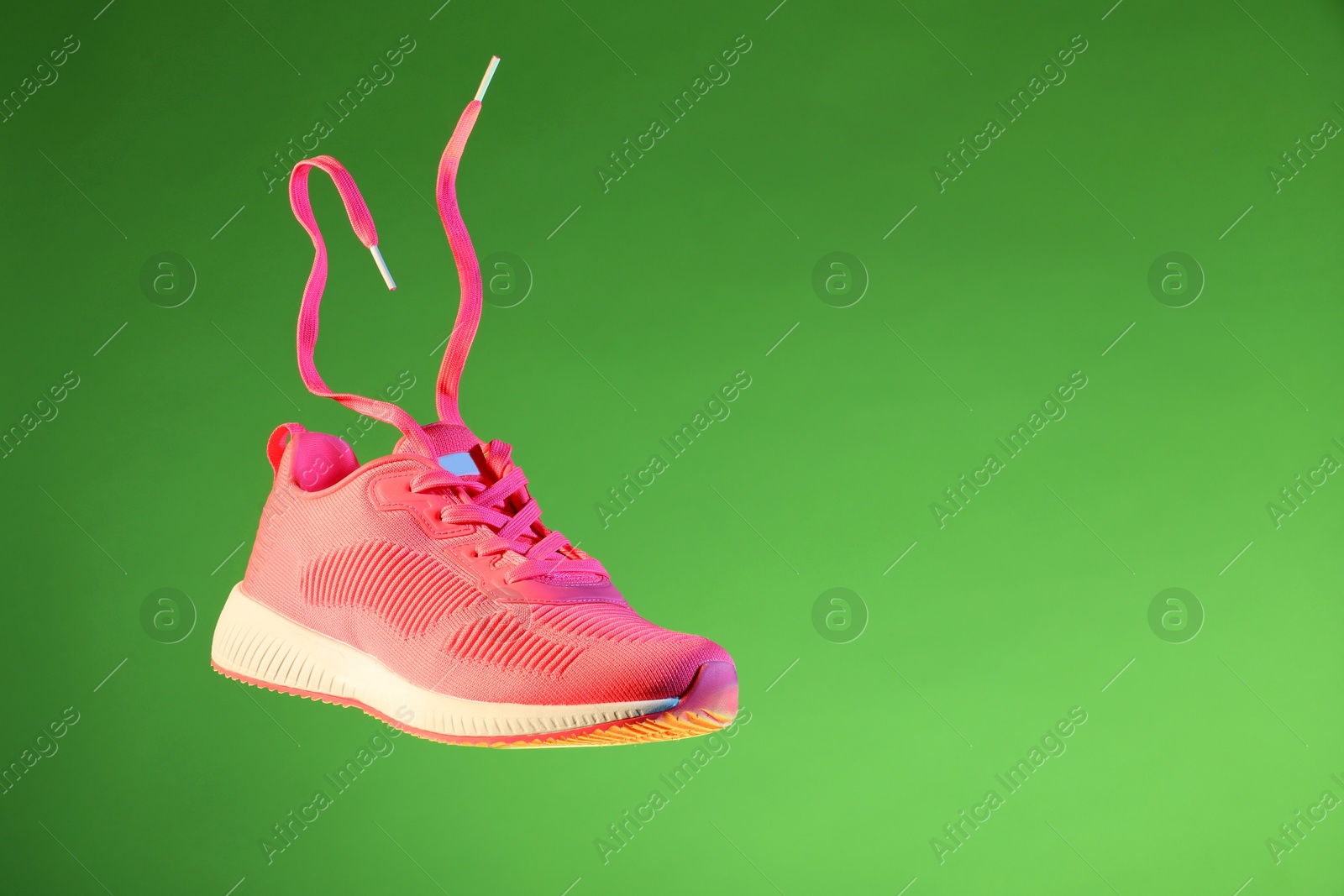 Photo of Stylish sneaker in air against green background, space for text