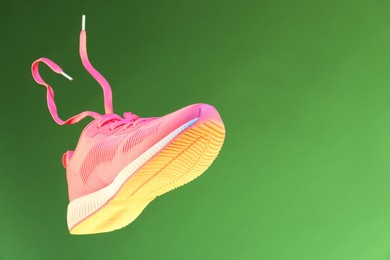 Photo of Stylish sneaker in air against green background, space for text