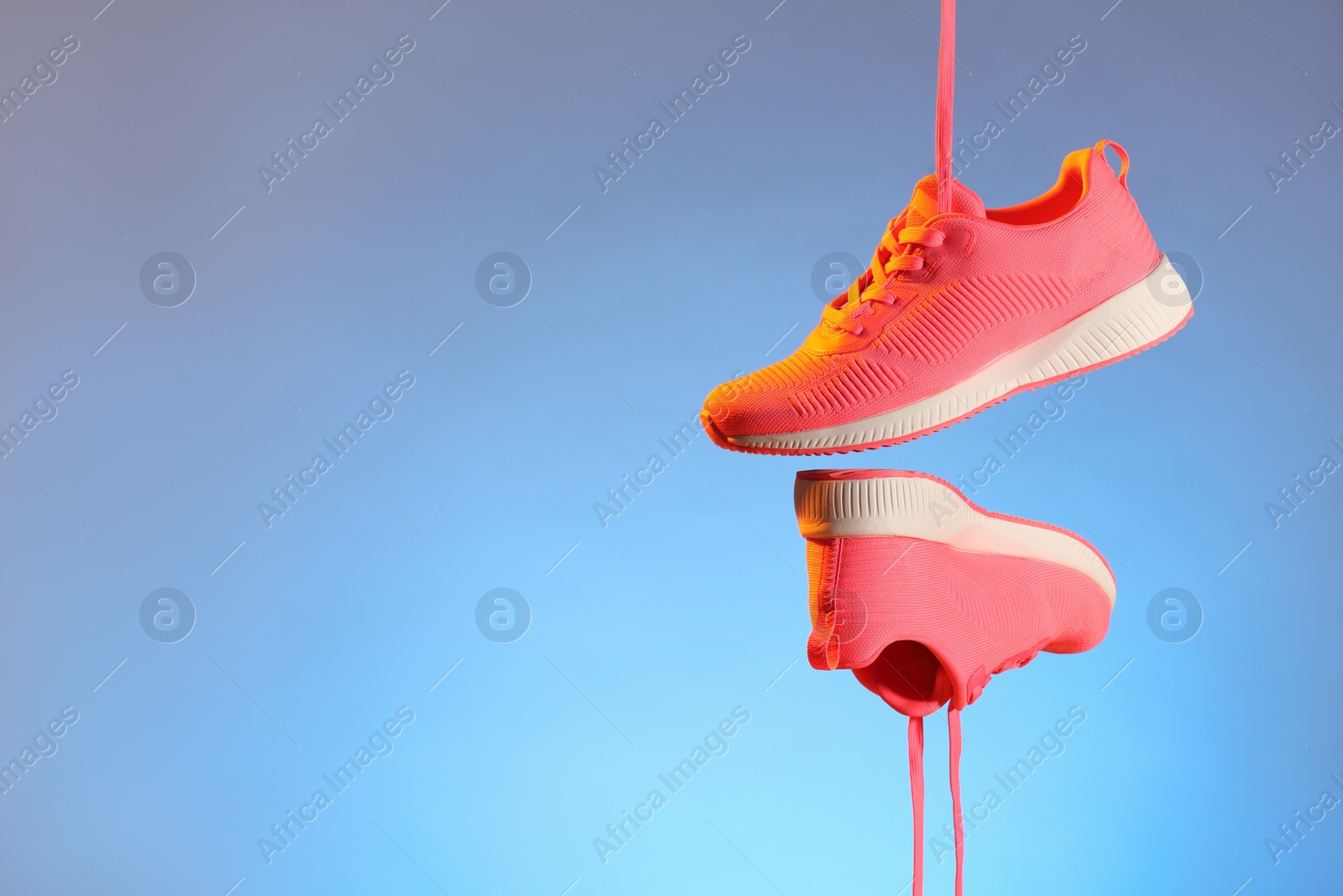 Photo of Pair of stylish sneakers in air against light blue background in neon lights, space for text