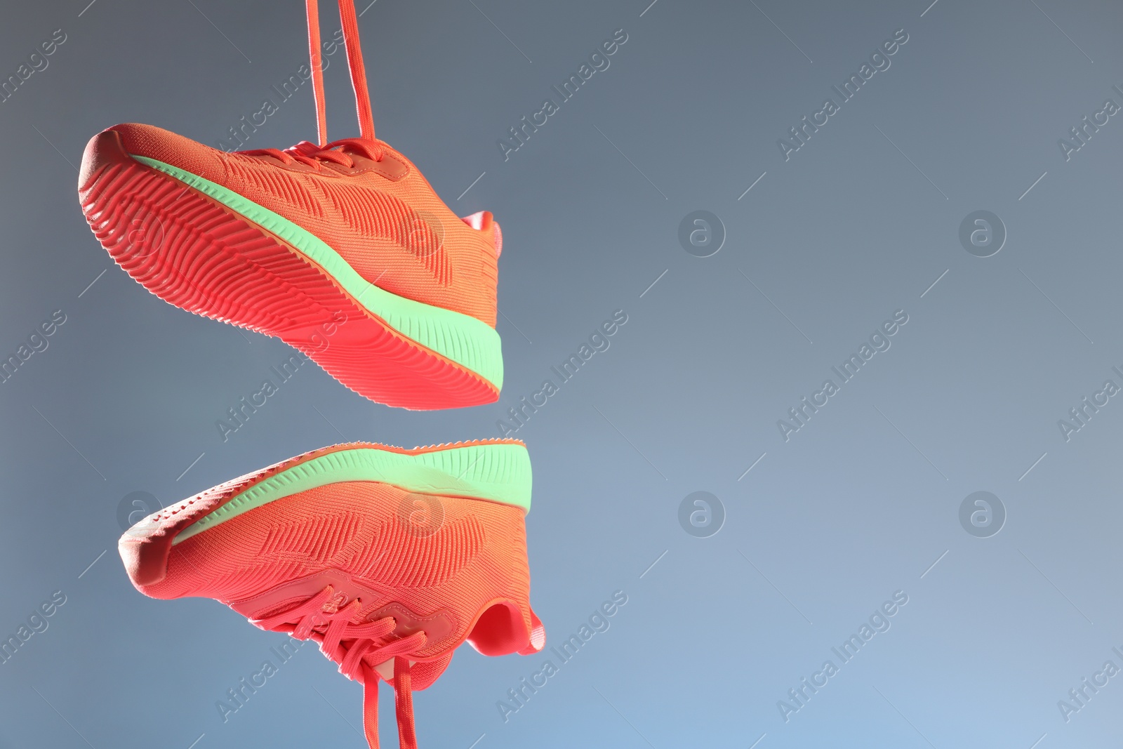 Photo of Pair of stylish sneakers in air against color background in neon lights, space for text