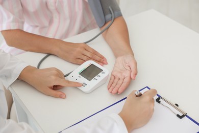 Doctor measuring patient's blood pressure at table in hospital, closeup