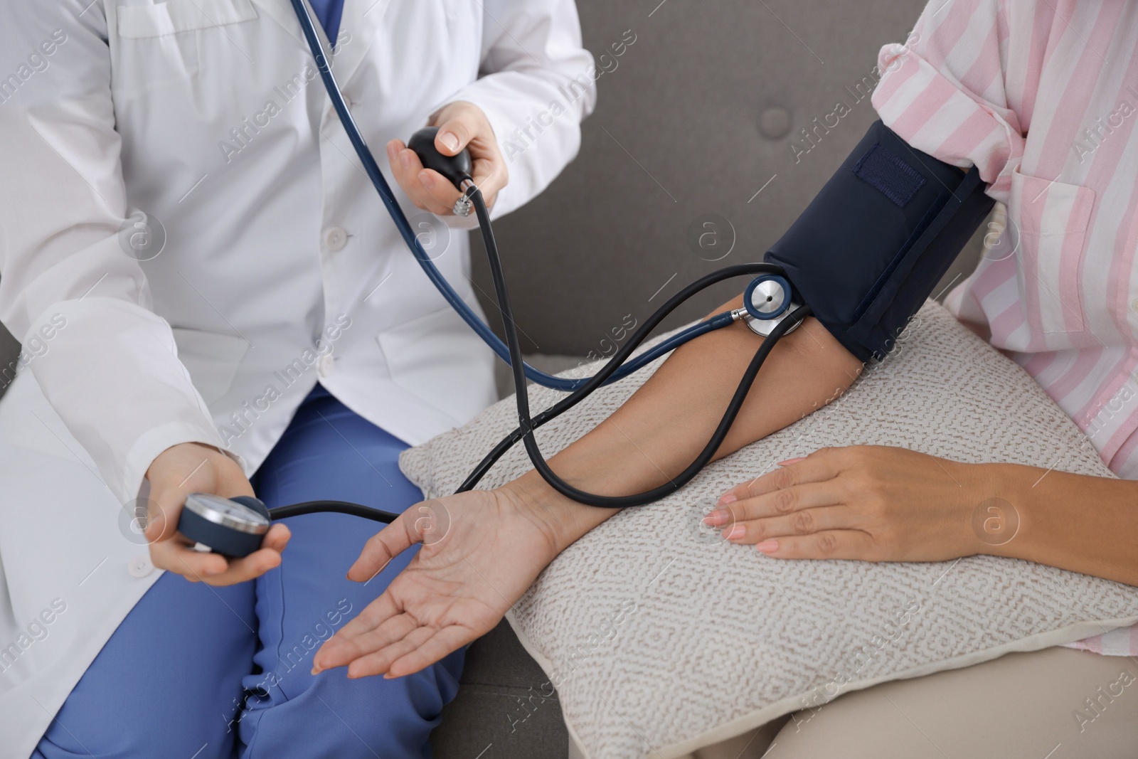 Photo of Doctor measuring patient's blood pressure on sofa indoors, closeup