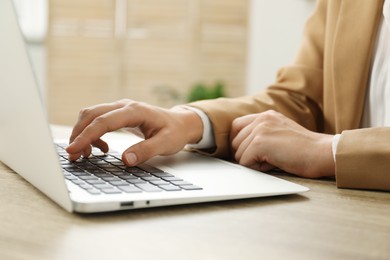 Photo of Businesswoman using laptop at wooden table indoors, closeup. Modern technology