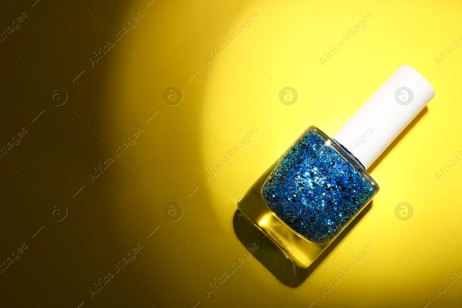 Photo of Nail polish in bottle on yellow background, top view. Space for text