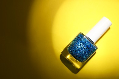 Photo of Nail polish in bottle on yellow background, top view. Space for text