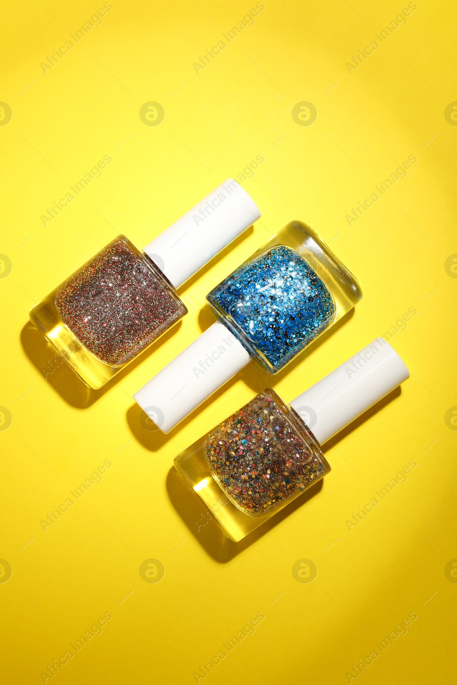 Photo of Nail polishes in bottles on yellow background, flat lay