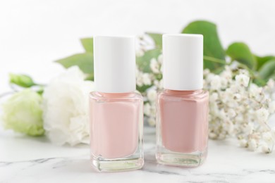 Photo of Nail polishes in bottles on white marble table, closeup