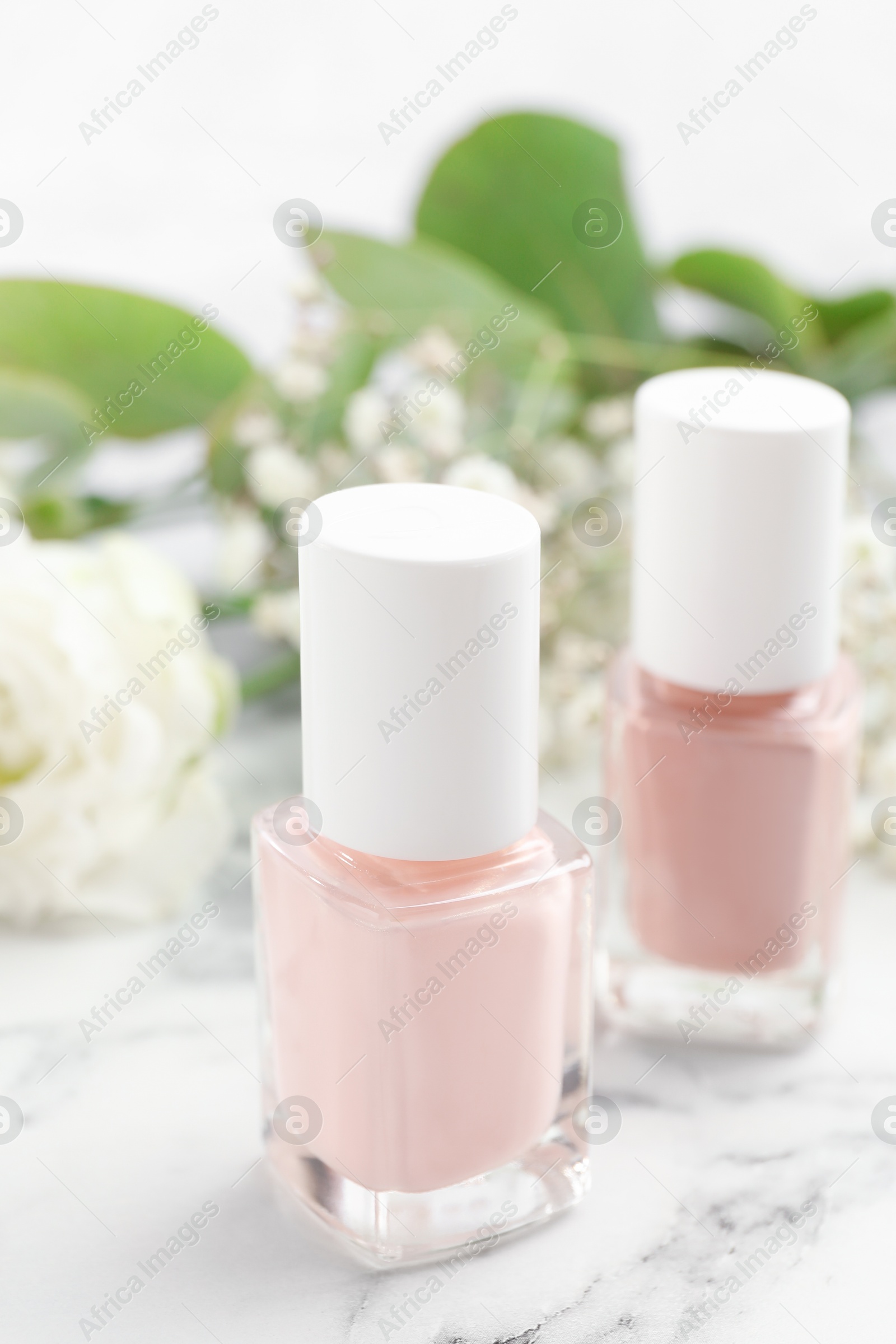 Photo of Nail polishes in bottles on white marble table, closeup