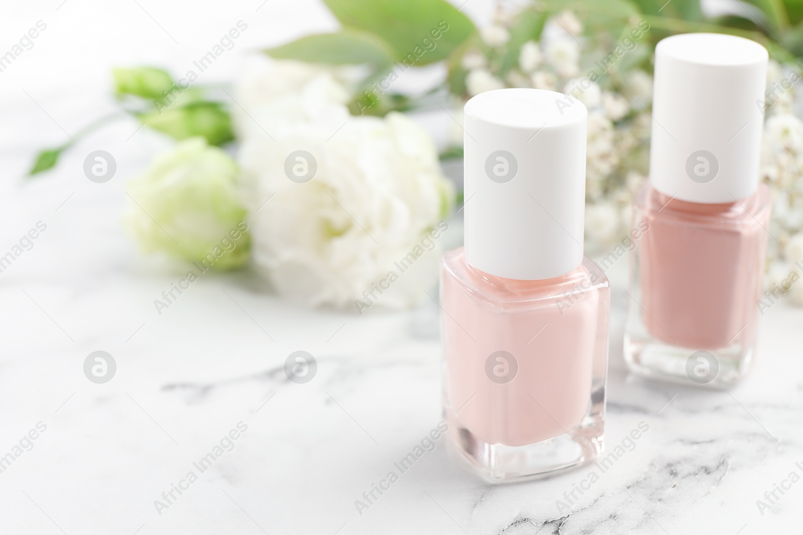 Photo of Nail polishes in bottles on white marble table, closeup. Space for text