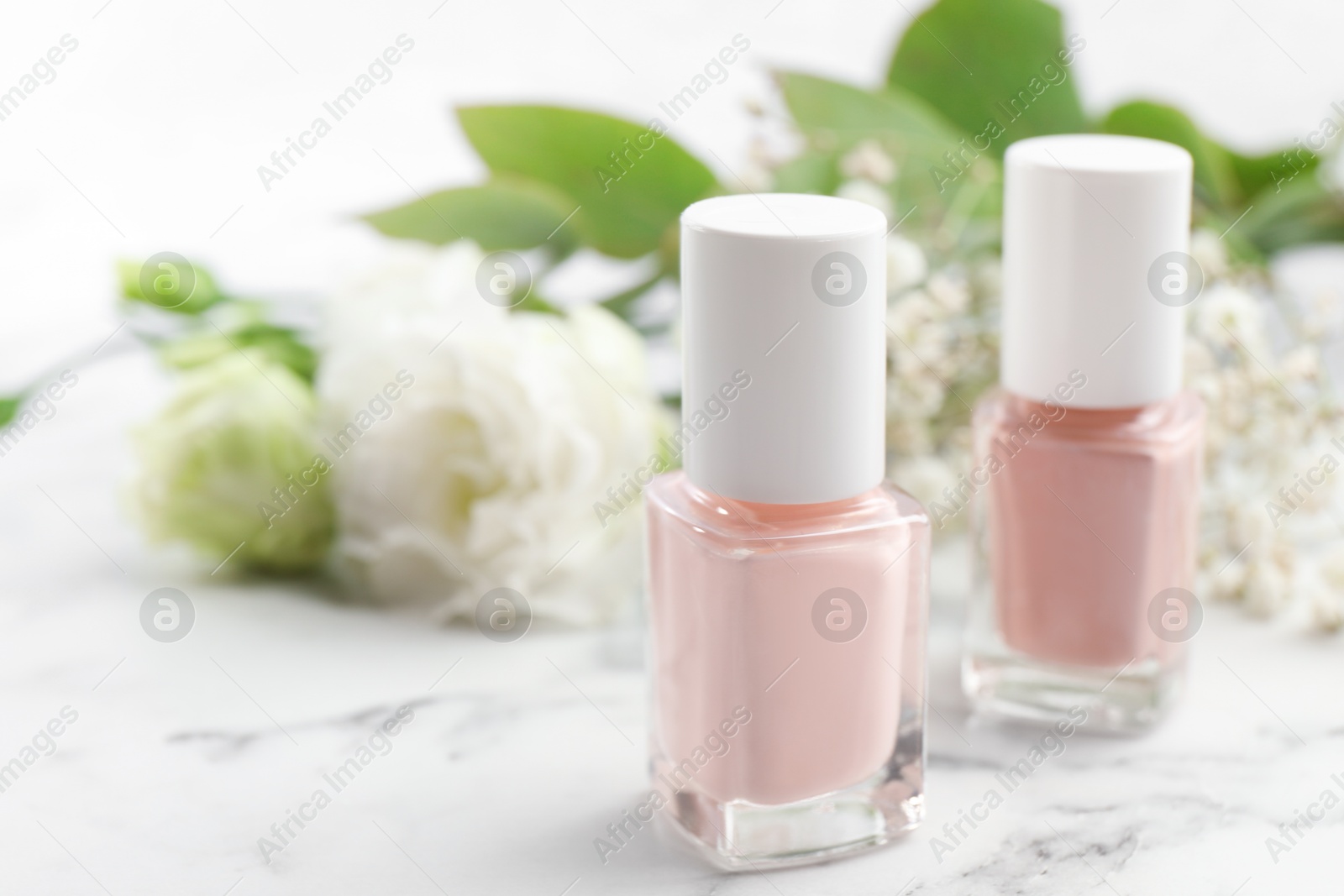 Photo of Nail polishes in bottles on white marble table, closeup. Space for text