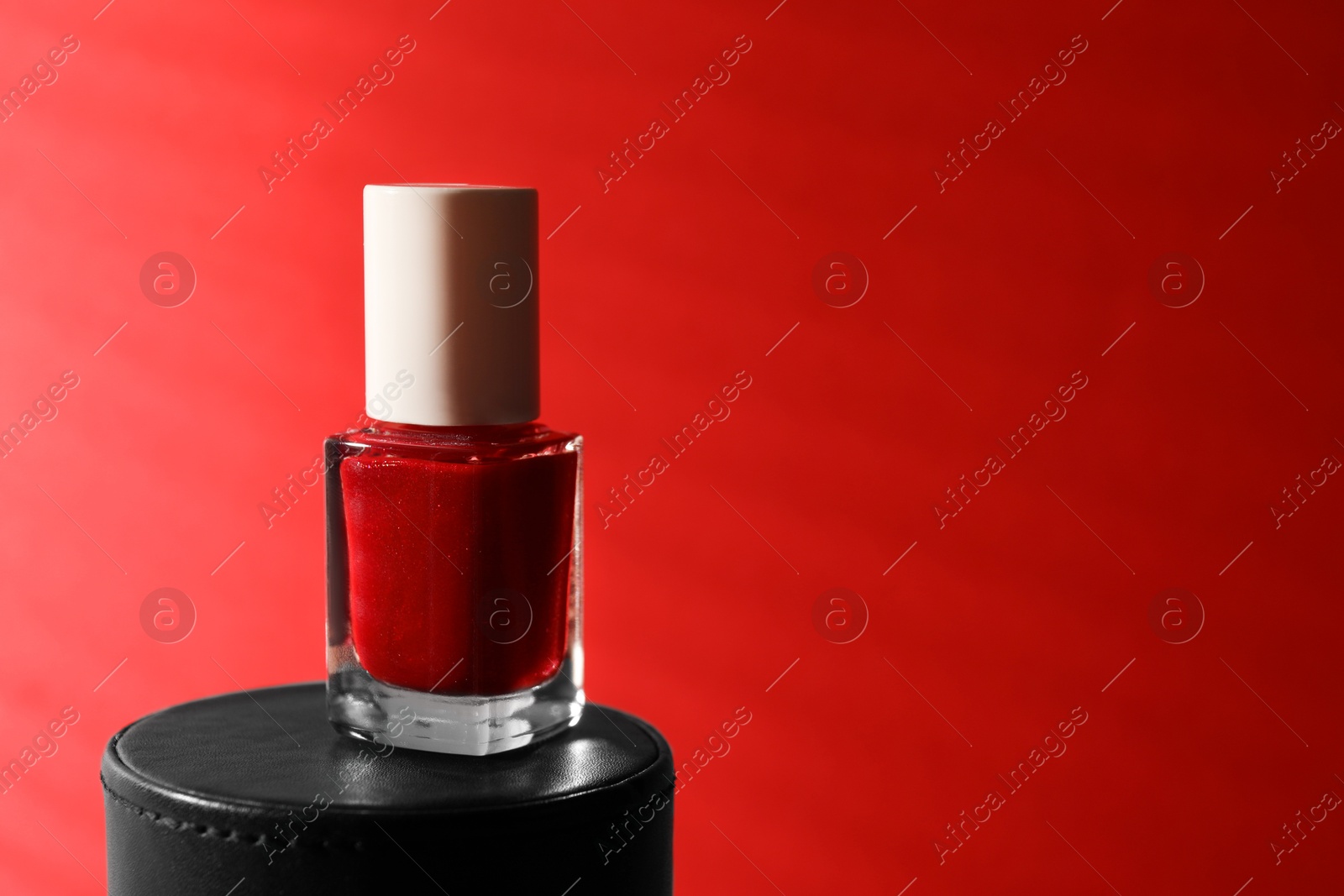 Photo of Nail polish in bottle on red background, space for text