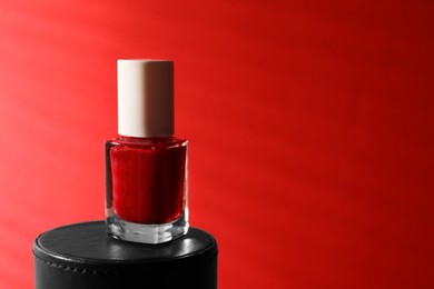 Photo of Nail polish in bottle on red background, space for text