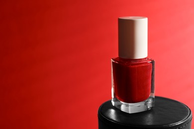 Photo of Nail polish in bottle on red background, space for text