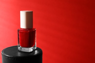 Photo of Nail polish in bottle on red background, space for text