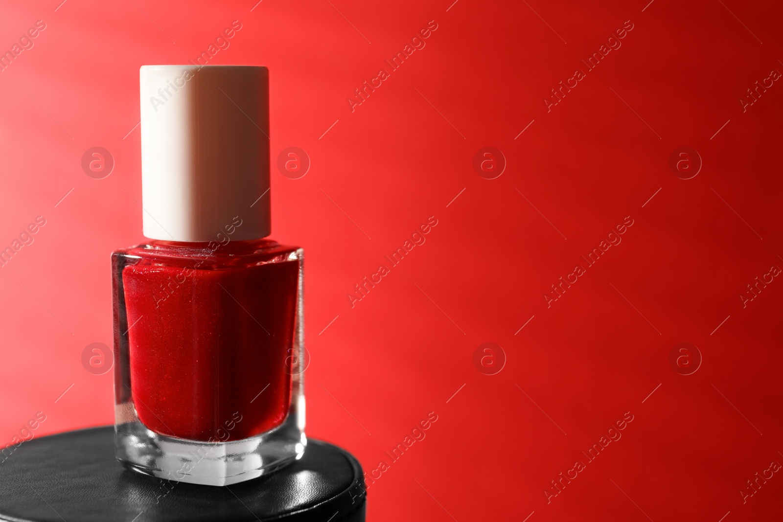 Photo of Nail polish in bottle on red background, space for text