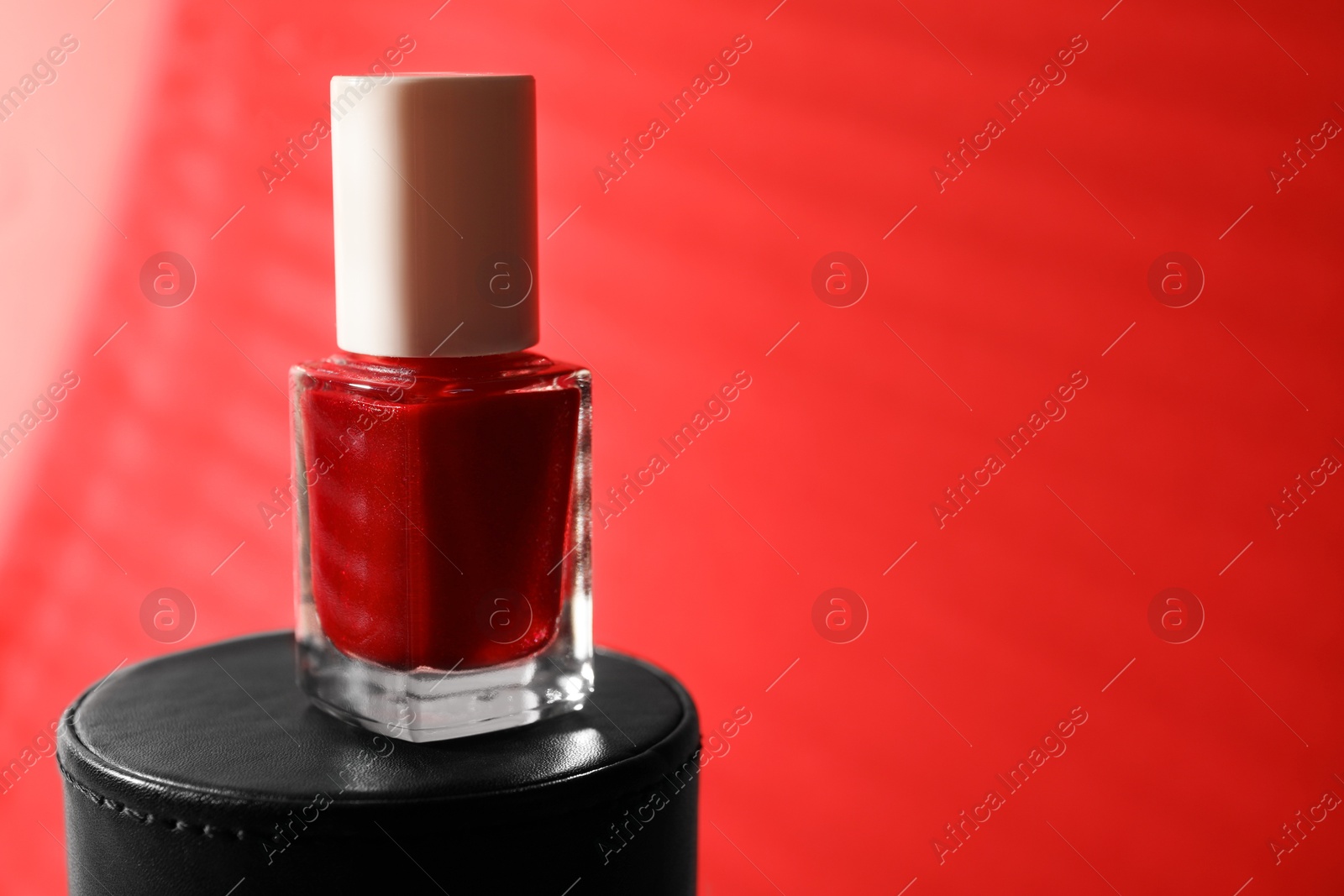 Photo of Nail polish in bottle on red background, space for text