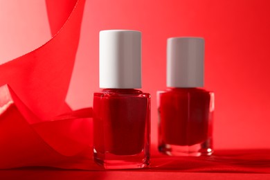 Photo of Nail polish in bottles on red background, closeup. Space for text