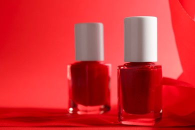 Photo of Nail polish in bottles on red background, closeup. Space for text