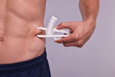 Photo of Man measuring body fat with caliper on grey background, closeup