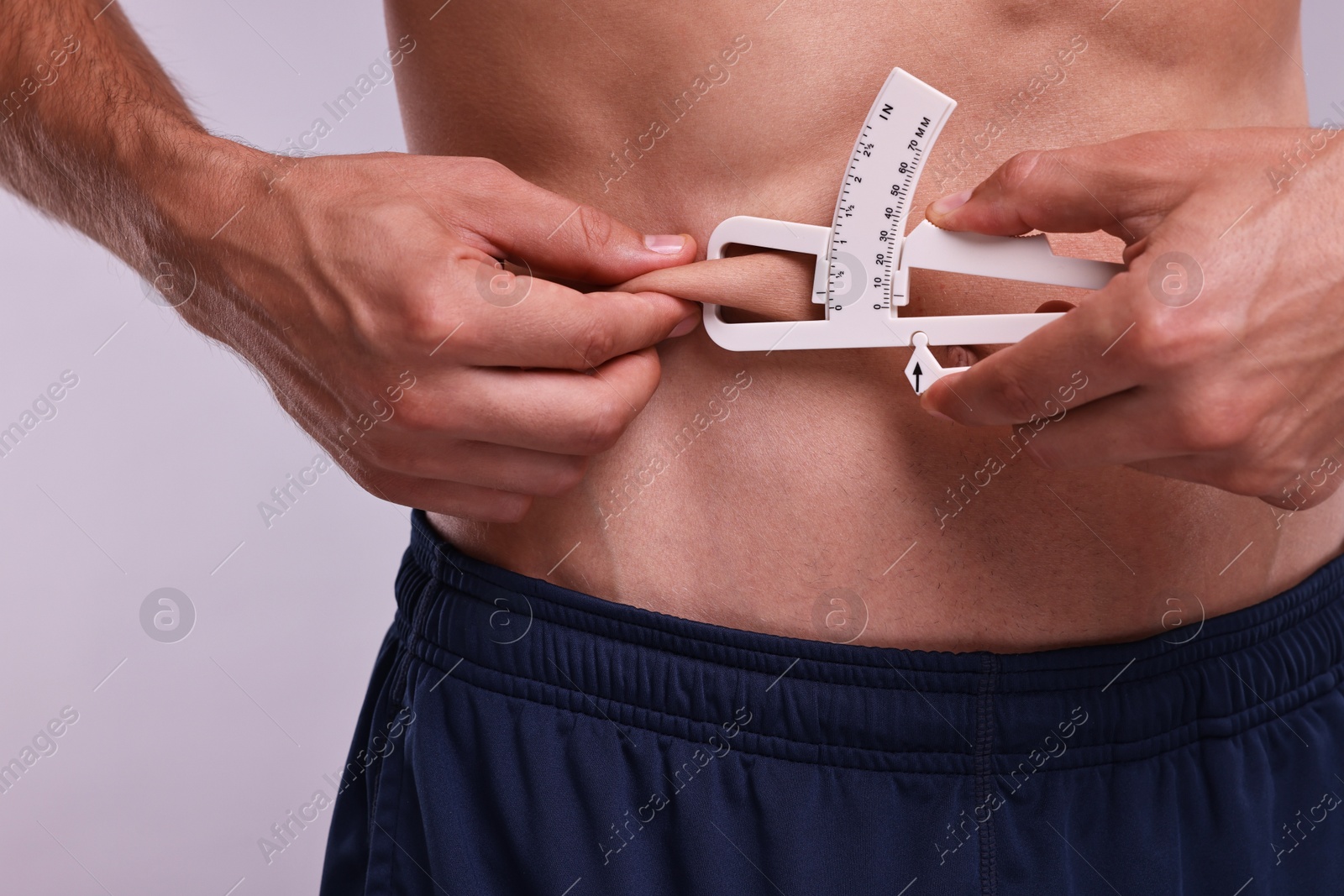 Photo of Man measuring body fat with caliper on grey background, closeup