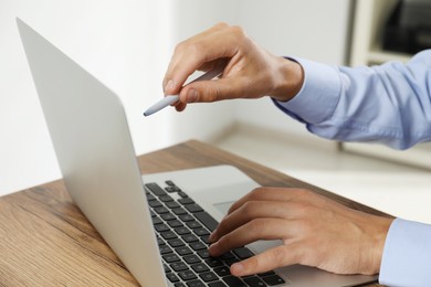 Photo of Businessman with pen using laptop at wooden table, closeup. Modern technology