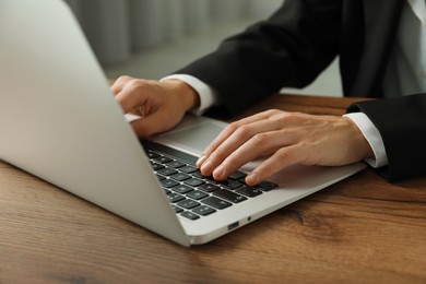 Photo of Businesswoman using laptop at wooden table indoors, closeup. Modern technology