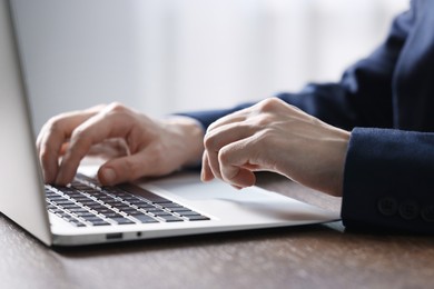 Photo of Businessman using laptop at table indoors, closeup. Modern technology