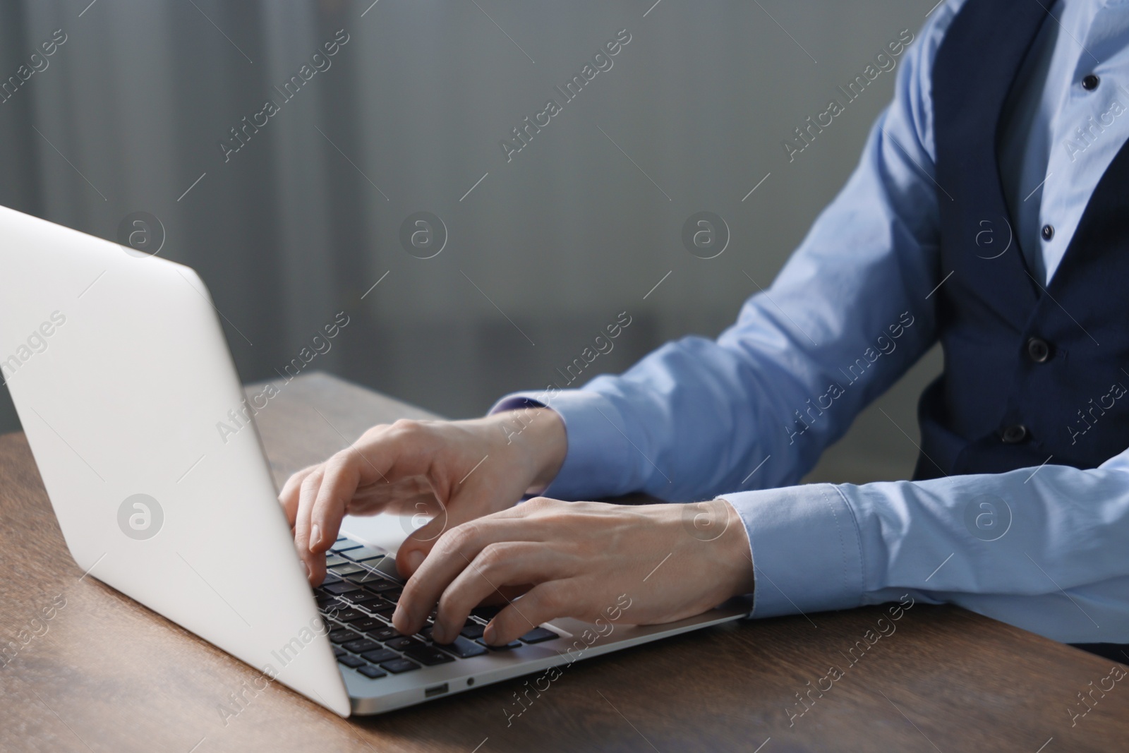 Photo of Businessman using laptop at wooden table indoors, closeup. Modern technology