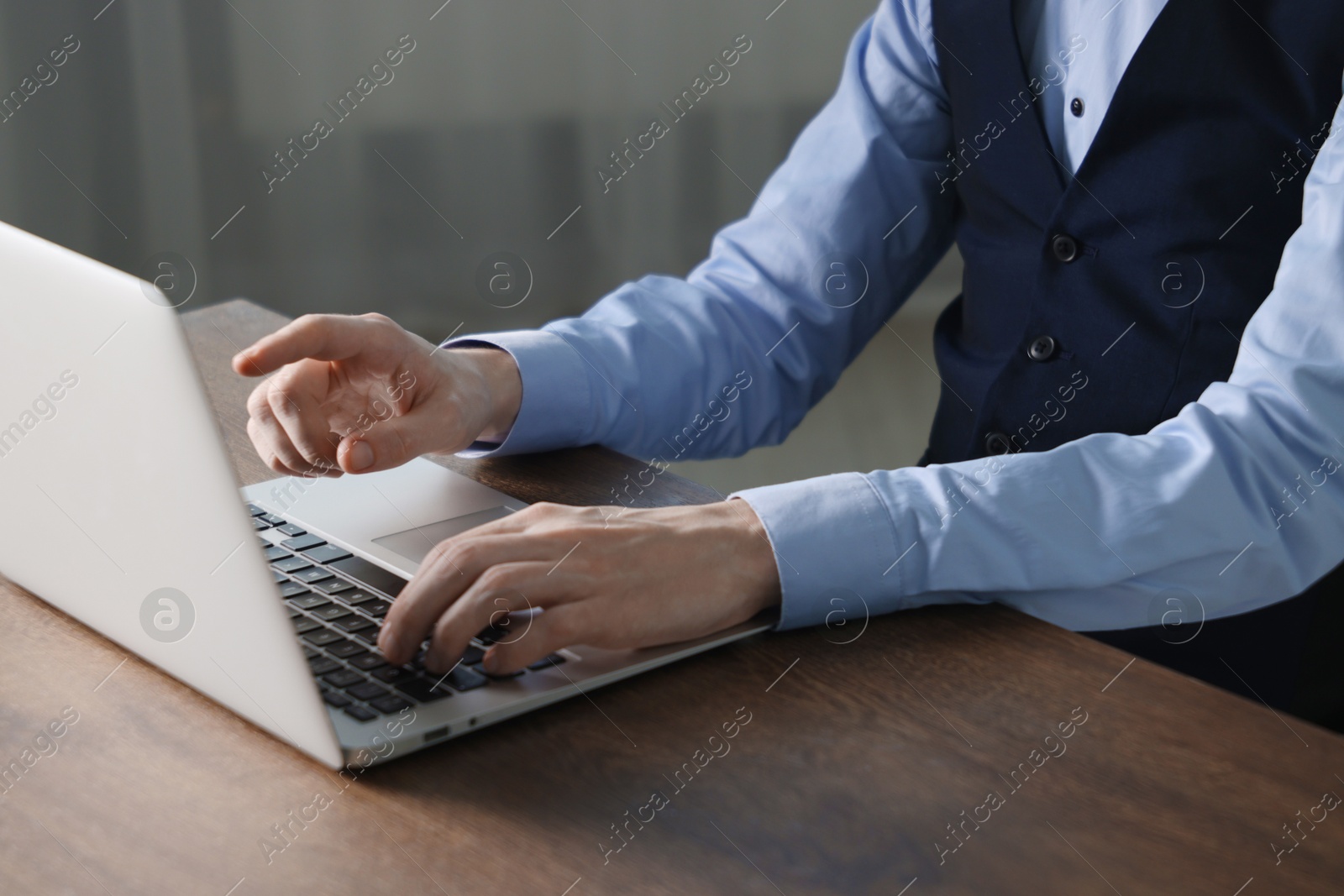 Photo of Businessman using laptop at wooden table indoors, closeup. Modern technology