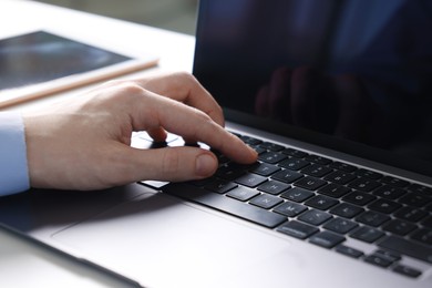 Photo of Businessman using laptop at white table indoors, closeup. Modern technology