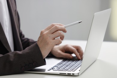 Photo of Businessman using laptop at white table indoors, closeup. Modern technology