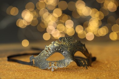 Photo of Beautiful carnival mask on golden shiny surface against blurred lights, closeup