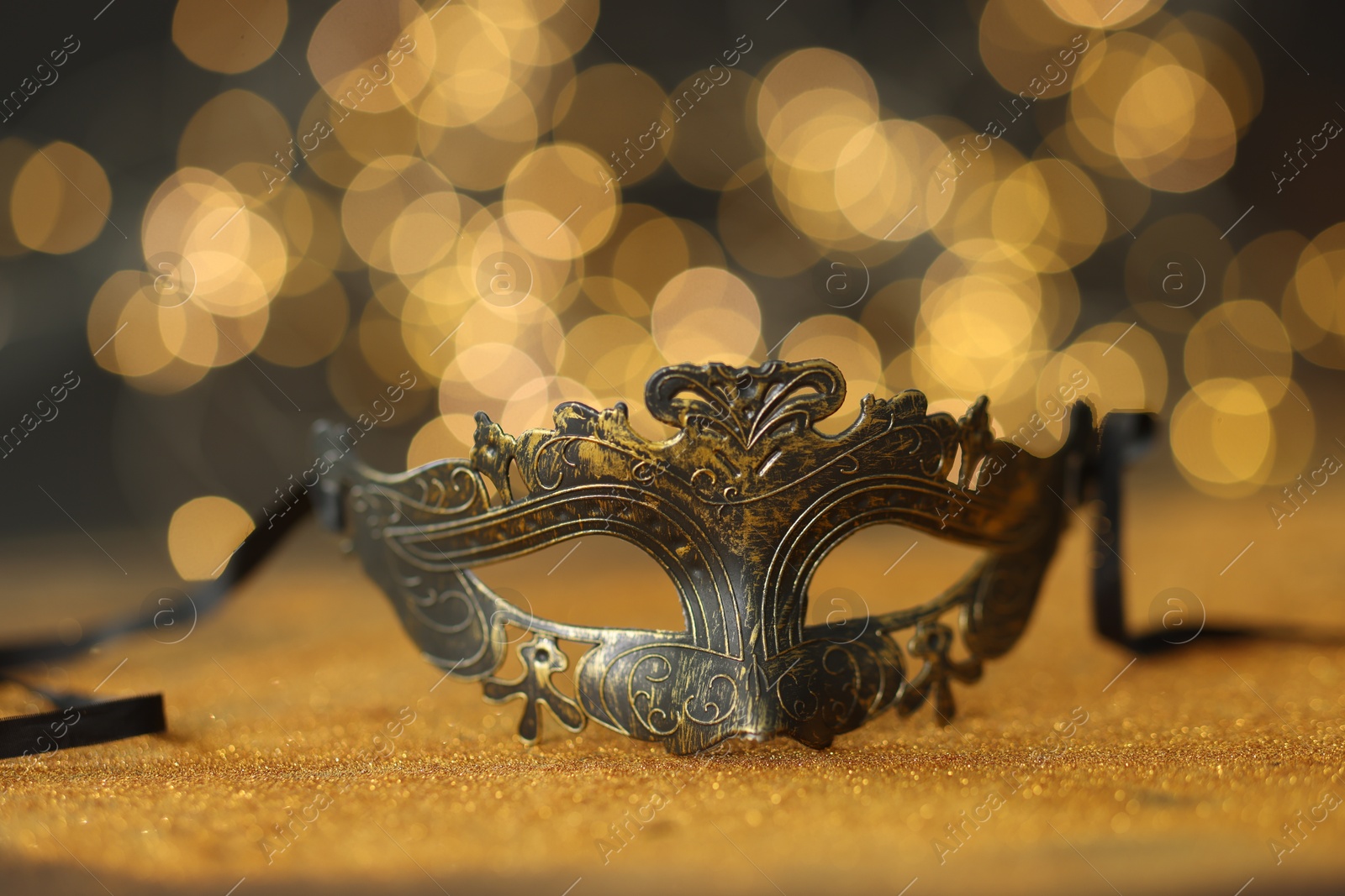 Photo of Beautiful carnival mask on golden shiny surface against blurred lights, closeup