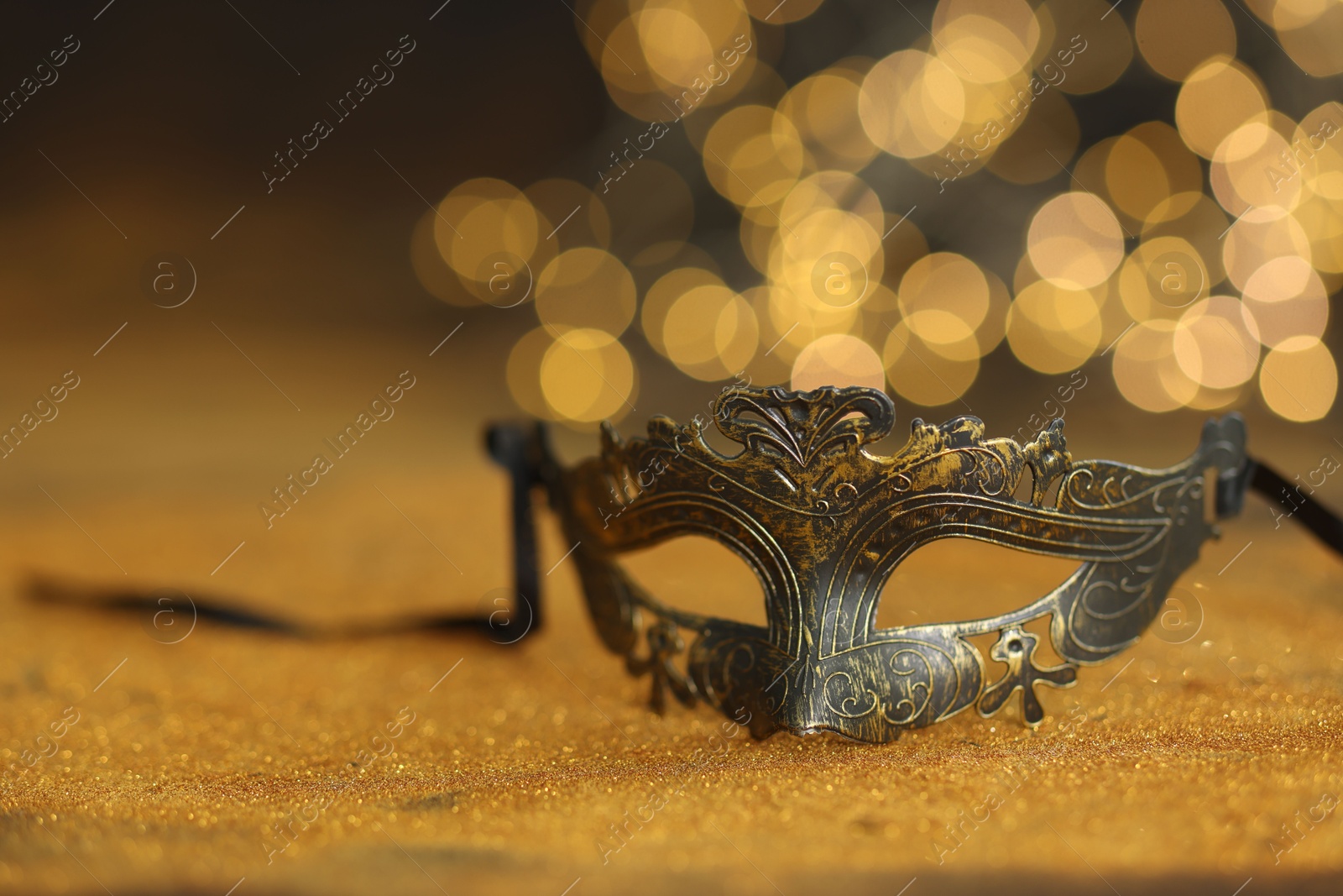 Photo of Beautiful carnival mask on golden shiny surface, closeup. Space for text