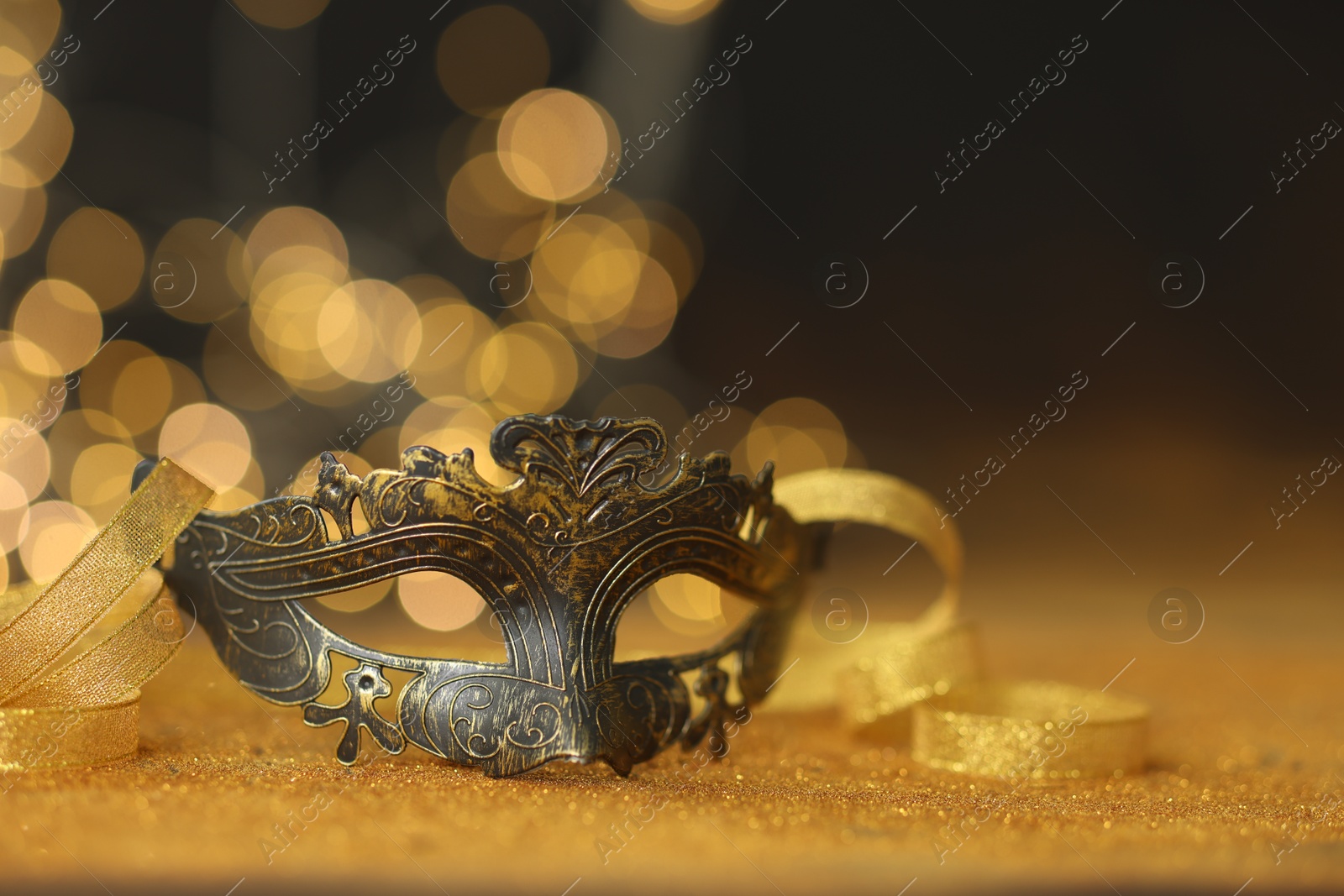 Photo of Beautiful carnival mask on golden shiny surface, closeup. Space for text