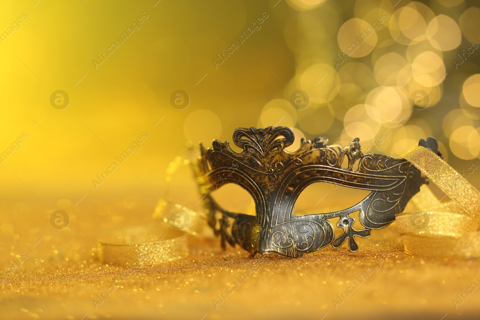 Photo of Beautiful carnival mask on golden shiny surface, closeup. Space for text