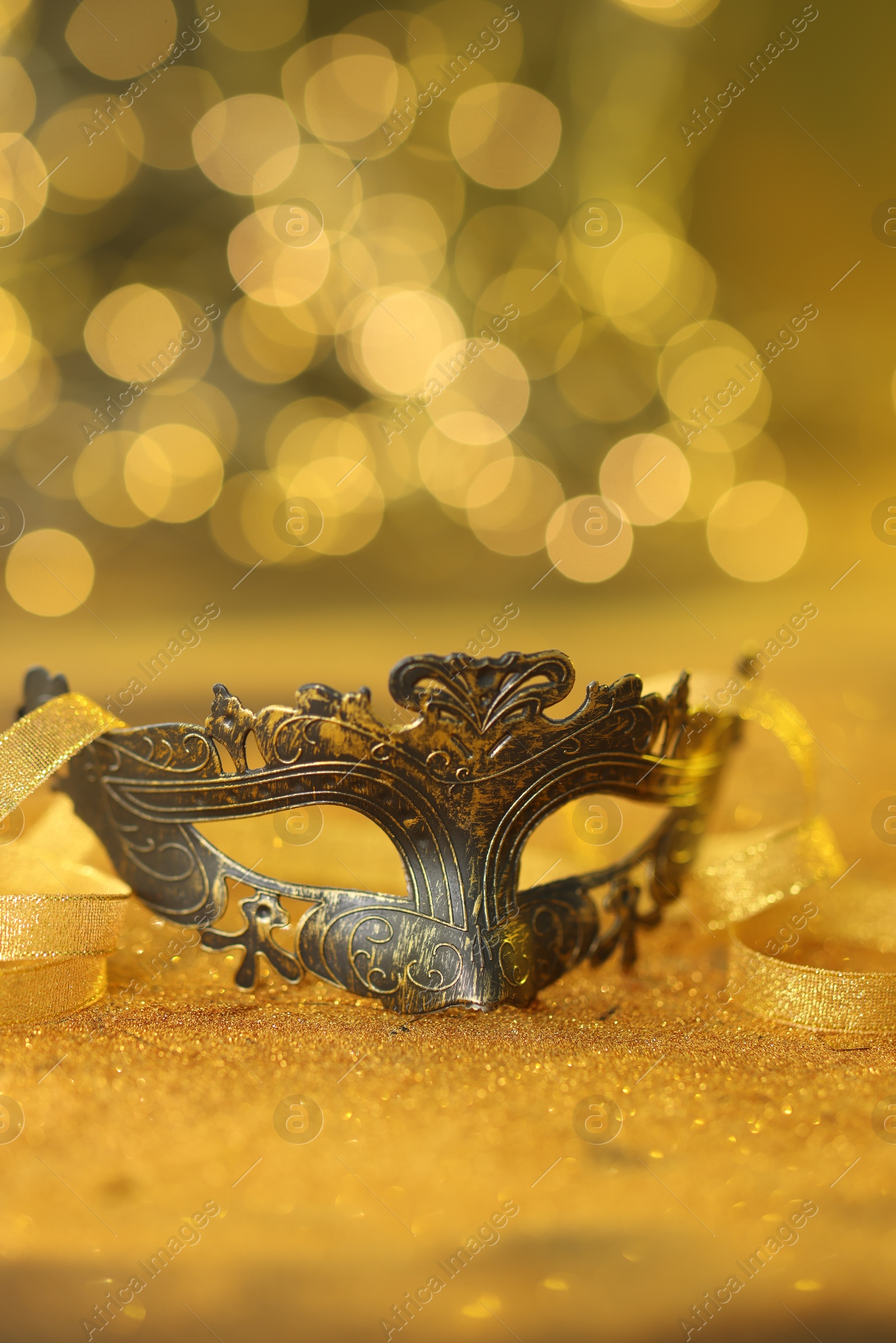 Photo of Beautiful carnival mask on golden shiny surface against blurred lights, closeup