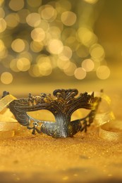 Photo of Beautiful carnival mask on golden shiny surface against blurred lights, closeup