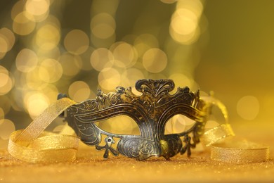 Photo of Beautiful carnival mask on golden shiny surface against blurred lights, closeup