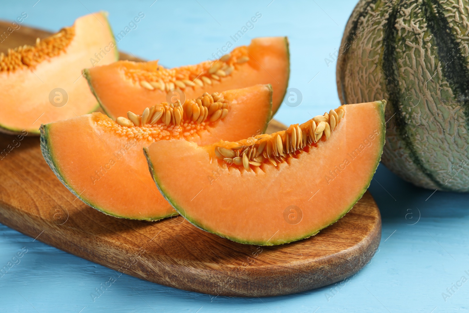 Photo of Tasty ripe Cantaloupe melon on light blue table, closeup