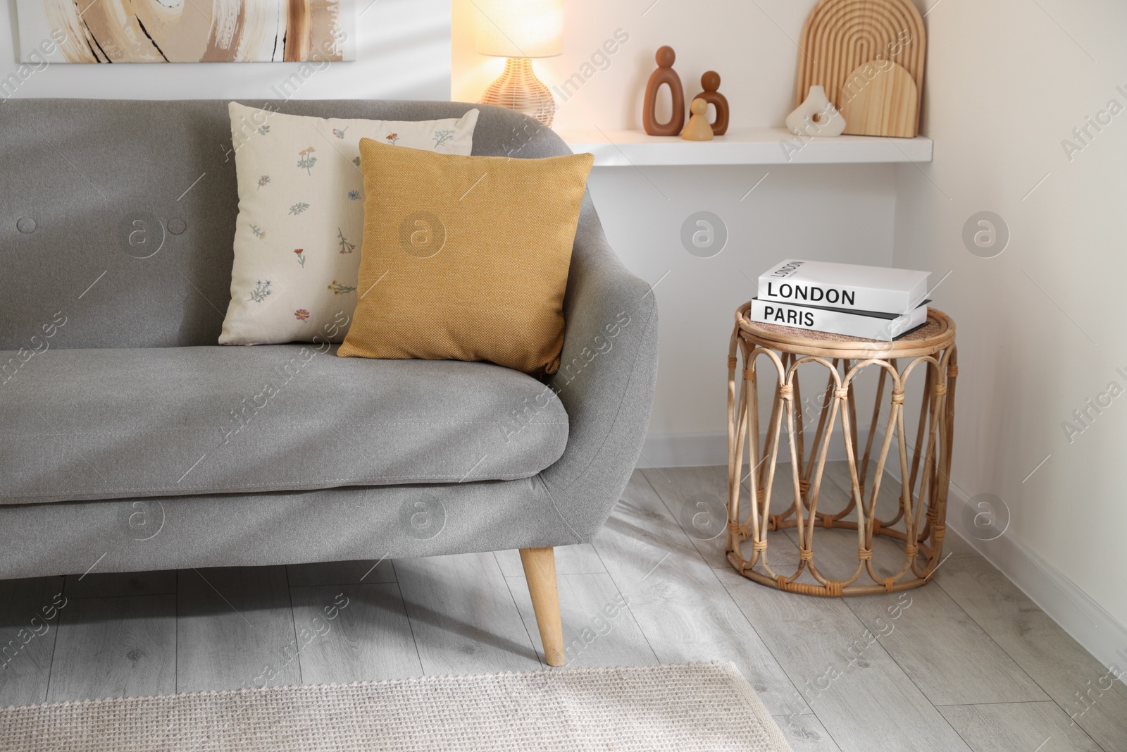 Photo of Different soft pillows on gray sofa and side table with books in living room